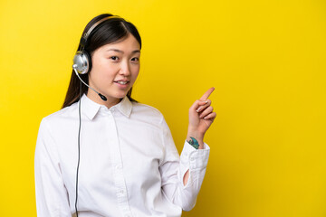 Telemarketer Chinese woman working with a headset isolated on yellow background pointing finger to...