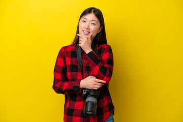 Young photographer Chinese woman isolated on yellow background smiling