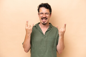 Naklejka premium Young caucasian man isolated on beige background making horn gesture