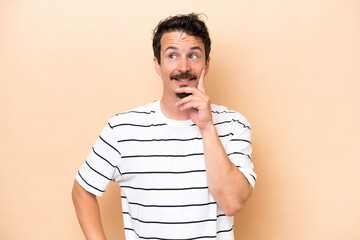 Young caucasian man isolated on beige background thinking an idea while looking up
