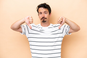Young caucasian man isolated on beige background showing thumb down with two hands