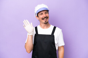 Fishmonger man wearing an apron isolated on purple background saluting with hand with happy expression
