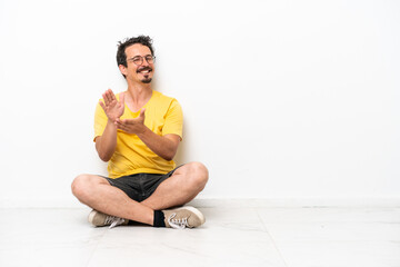 Fototapeta premium Young caucasian man sitting on the floor isolated on white background applauding after presentation in a conference