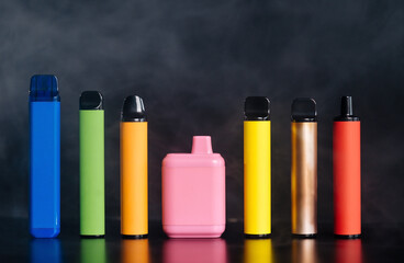 A set of colorful disposable electronic cigarettes of different shapes on a black background with...