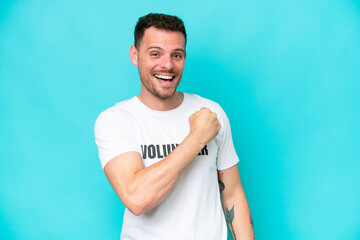 Fototapeta premium Young volunteer caucasian man isolated on blue background celebrating a victory