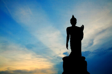 Silhouette standing buddha statue against blue sky and rays of light