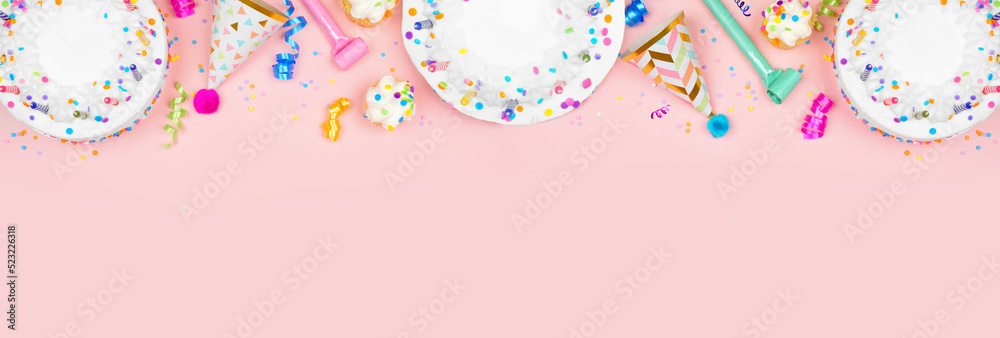 Wall mural Birthday party top border on a pink banner background. Above view with cakes, party hats and confetti. Copy space.