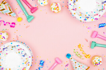 Birthday party frame on a soft pink background. Top view with cakes, party hats and confetti. Copy space.