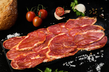 Iberian loin slices on black slate with tomato, parsley, peppercorns and a slice of mushroom