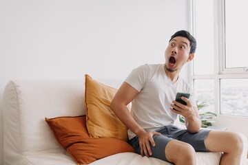 Shocked and Surprised asian man using smartphone looking at the empty space.