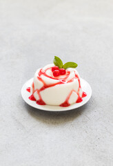 Vanilla cream pudding, Panna Cotta in the shape of a rose, with red currant sauce, on a plate. Light grey background