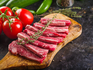 Cooking steaks from organic meat from the farm. On a wooden cutting board, pieces of steaks with a sprig of rosemary, vegetables on a dark background. Meat recipes.