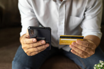 Man holding credit card and using smartphone at home, businessman shopping online, e-commerce, internet banking, spending money, working from home concept, Sit on the sofa in the living room at home.