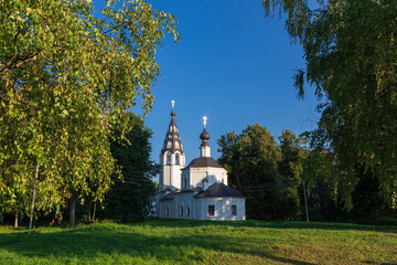 Fototapeta na wymiar Russian Orthodox church amond big trees framed with birch foliage against clear sky, Plyos, Russia