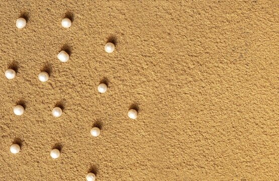 Pearls pattern on the sand with copy space. A creative wedding concept with white pearl. Summer background with pearls on the sand.