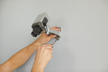 Hands master man with screwdriver mount camera for surveillance in anti-vandal metal case designed for protection and security on wall inside building. Video CCTV system for business concept