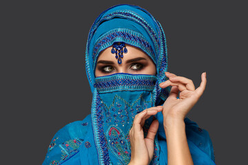 Studio shot of a young beautiful woman wearing the blue hijab decorated with sequins and jewelry. Arabic style.