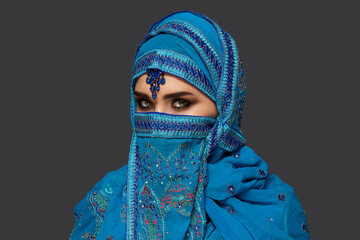 Studio shot of a young beautiful woman wearing the blue hijab decorated with sequins and jewelry. Arabic style.