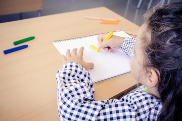 little girl drawing with colored pencils or crayons on a table at school