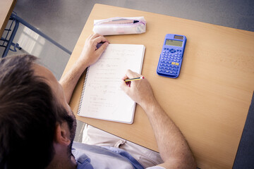 boy doing homework in class using calculator and pencil on a table