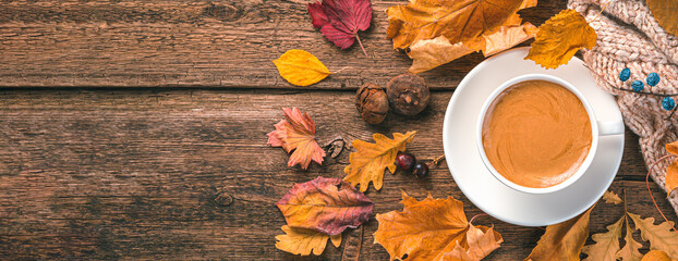 Coffee mug, sweater and foliage on a wooden background. Top view, copy space. Autumn background