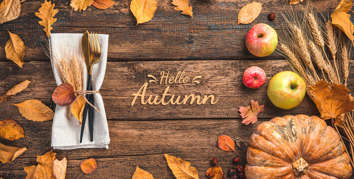 Festive autumn background with cutlery, pumpkin, apples and autumn foliage on a wooden table. Top view, copy space