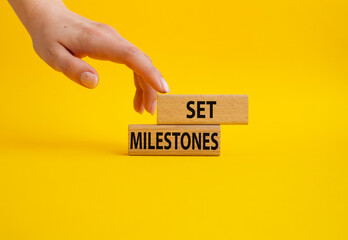 Set milestones symbol. Concept word Set milestones on wooden blocks. Beautiful yellow background. Businessman hand. Business and Set milestones concept. Copy space