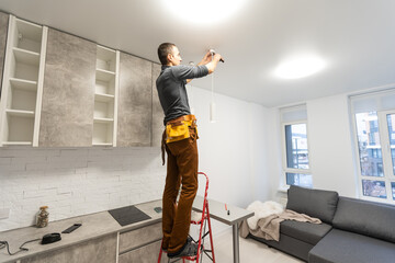 electrician, a male electrician is standing on the stairs holding wiring in his hands and stripping, repairing light at home, repair work, call master, electrician man repairing light
