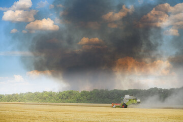Combine harvester against the backdrop of black smoke rising into the sky.
