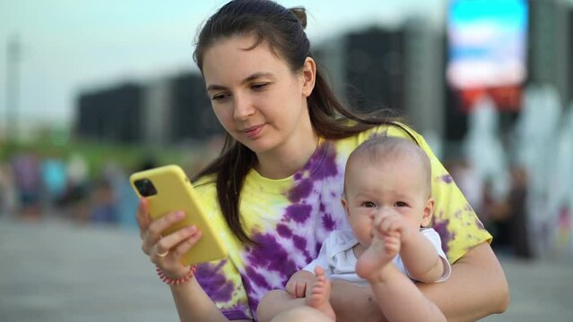 Child boy with mom relaxing outdoor in the city center. Woman using cellphone