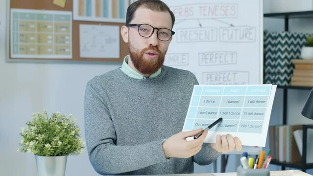 Joyful young man teaching English online speaking and showing chart enjoying distant education. Modern technology and people concept.