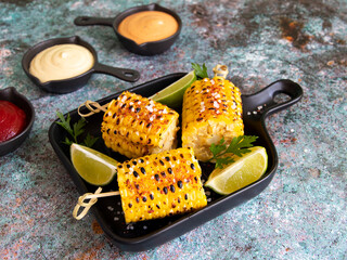 grilled yellow corn with spices lime with white red orange sauce portion