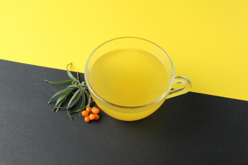 sea buckthorn tea drink on black yellow background. Sea buckthorn juice glass cup next to a spout of sea buckthorn leaves orange berries on a black and yellow background. creative photography. 