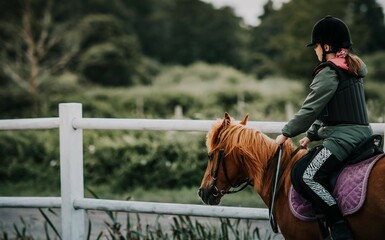 Dziewczynka jeździ konno w szkółce jeździeckiej. Obóz konny, ćwiczenia w siodle na padoku - obrazy, fototapety, plakaty