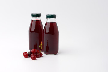 Two glass bottles with a cherry drink on a white background. Nearby cherry berries. Copy space.