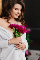 A gentle and peaceful brunette woman in white clothes with a bouquet of peonies.