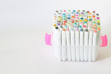 Lots of multi-colored numbered felt-tip pens or drawing markers in clear plastic box or case. White background. Concept of tools for artistic work, the development of creative abilities.