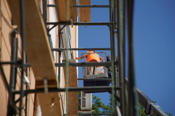 The plasterer worker in the telehandler work platform is visible through the scaffolding next to...