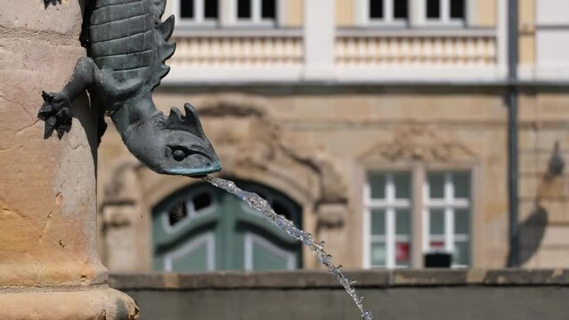 Fountain with bronze reptile statue on the market square of Eisenach, Germany. Close-up view of an animal shaped tap and clear fresh water against historic buildings. Translucent flowing water. 4K