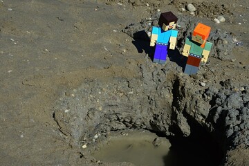 Fototapeta premium LEGO Minecraft large figures of Alex and Steve characters are looking on large wet muddy pit or crater on black sand beach with dirty water on bottom. Summer daylight sunshine.