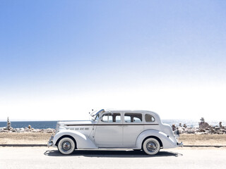 Fototapeta na wymiar Vintage old car along the beach in Malibu. Pacific Ocean in the background. Balancing Rocks to the side. White Packard vehicle.