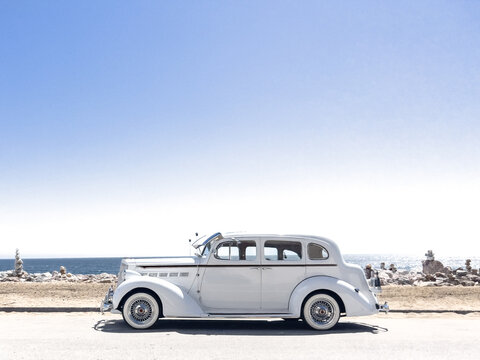 Vintage old car along the beach in Malibu.  Pacific Ocean in the background.  Balancing Rocks to the side.  White Packard vehicle.