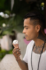 Young handsome mexican tattooed man eating ice cream in a waffle cone.