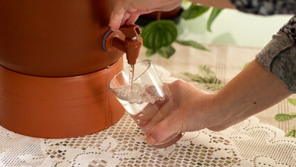 Woman filling a glass of water from a clay water filter (filtro de água de barro), common in...