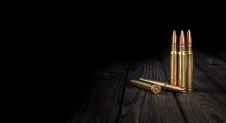Carbine and rifle cartridges stand on a wooden surface. Ammunition for weapons. Dark back.