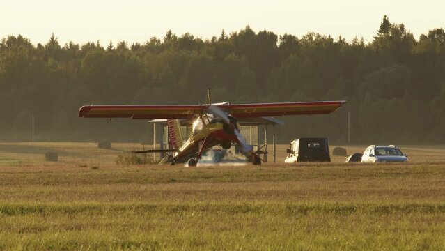 small yellow and red private jet starts engine, propeller start spin, there is lot of smoke around aircraft. shot was taken at dawn or dusk.