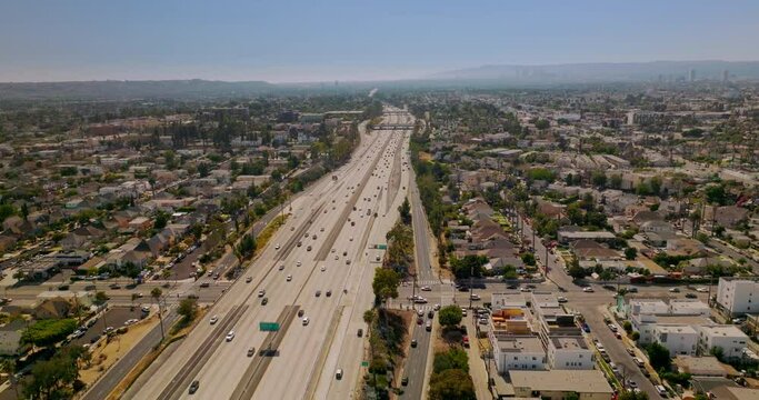 Multi-lane highway with numerous cars going through the big city. Sunny picture of Los Angeles from aerial view.