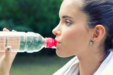 Young woman drinking water after exercise in summer nature