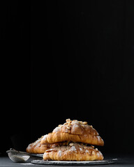 Baked croissant on a  board and sprinkled with powdered sugar, black table. Appetizing pastries for breakfast.