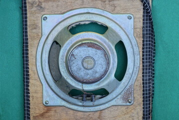 one big round old gray metal speaker on a brown wooden board lies on the green table 